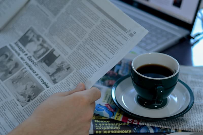 Person reading a newspaper with a cup of coffee